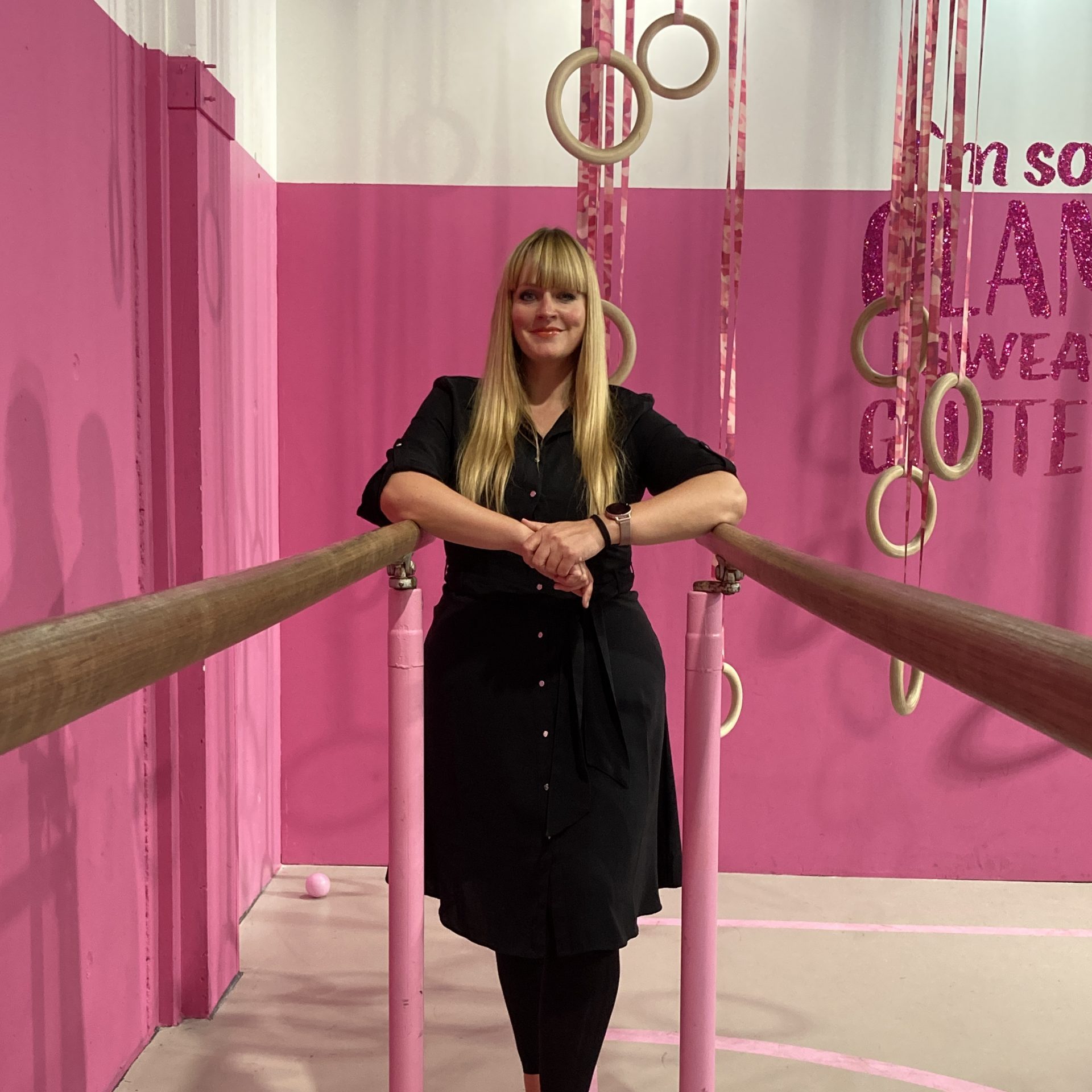 Daniela Friedrich steht vor einem pinken Hintergrund an einem Barren.